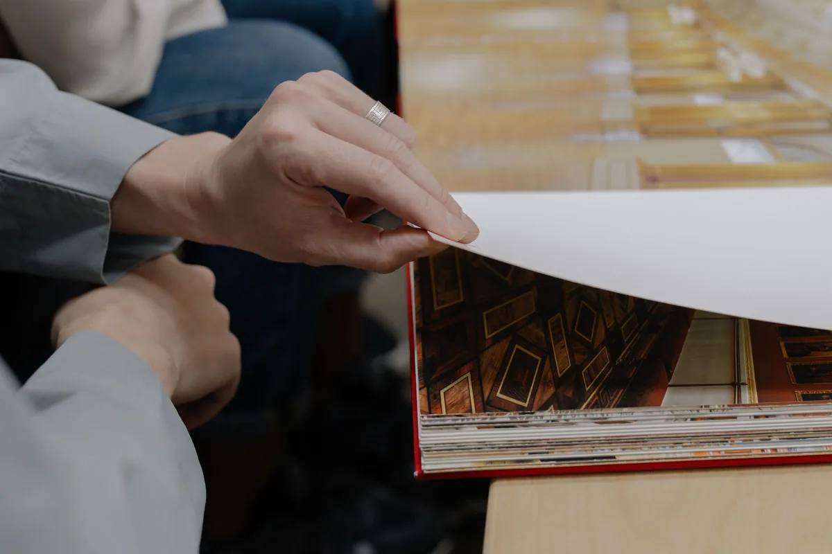 Hands lifting a printed proof sheet to check a page in a bound book