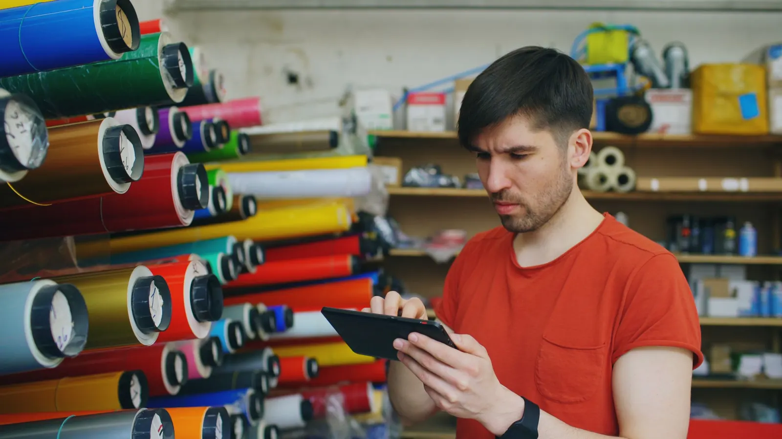 A sign maker checking a job on a tablet in front of rolls of coloured vinyl