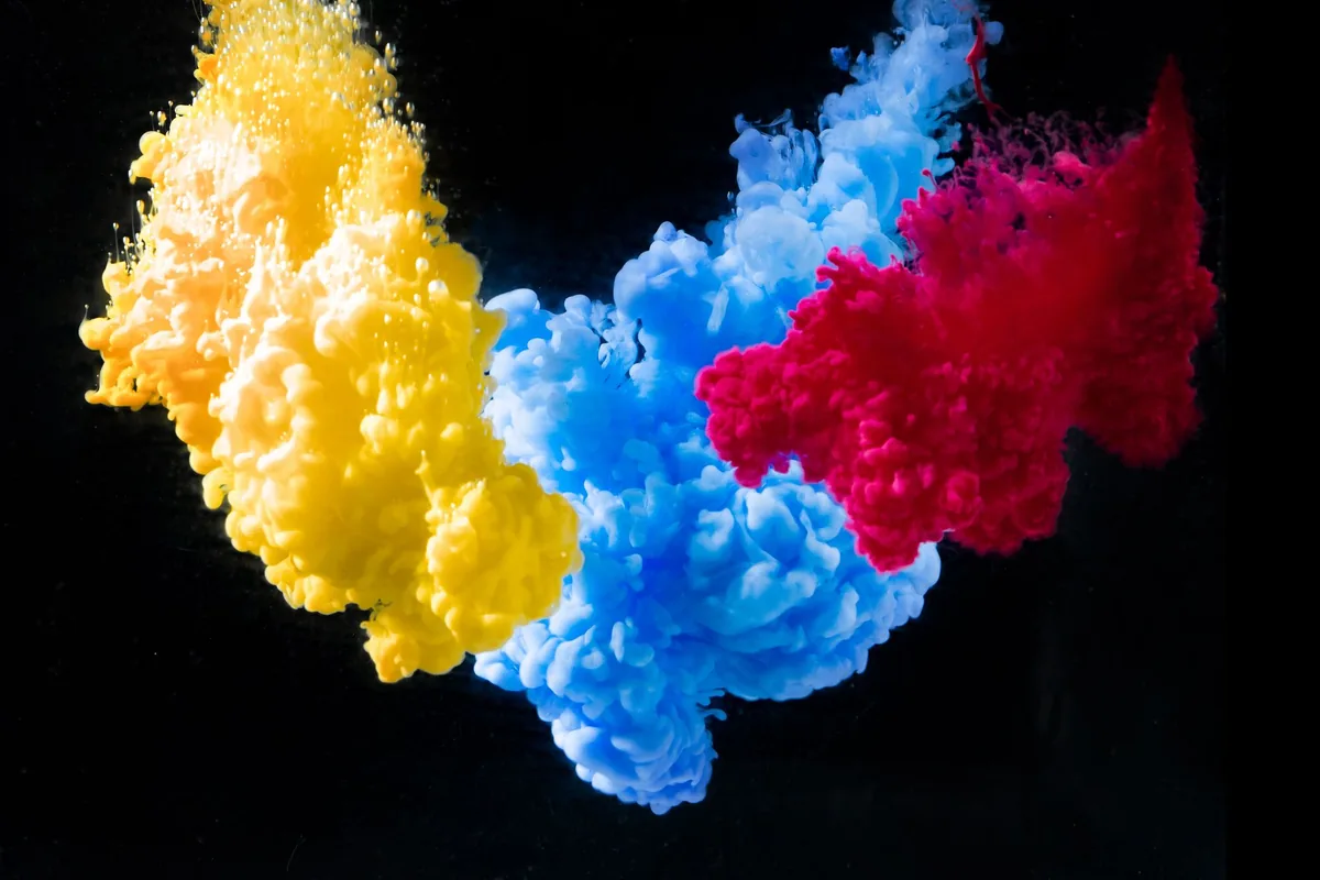 Yellow, cyan and magenta ink clouds mixing in water against a black background