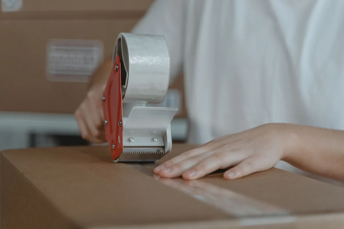 Hands sealing a cardboard parcel with a tape dispenser